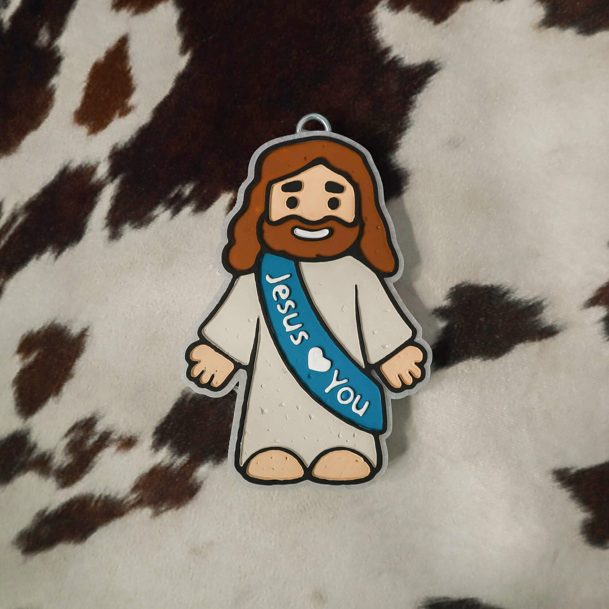 Cartoon character of a bearded figure with a 'Jesus Loves You' sash on a cowhide background